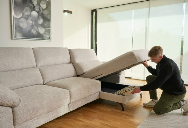 Sofá deslizante modelo LON en forma de L, color beige, en un salón con un hombre abriendo el espacio de almacenamiento